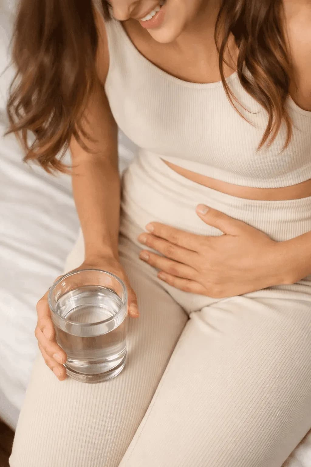 A woman holding a glass of water and touching her stomach